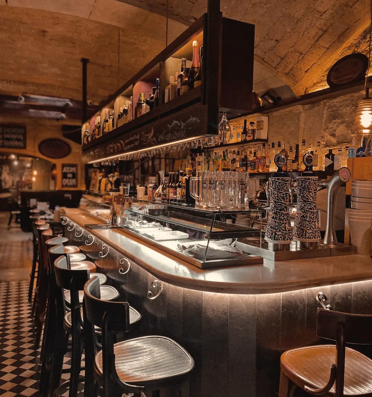 A bar counter at night, glasses lined up under warm lights