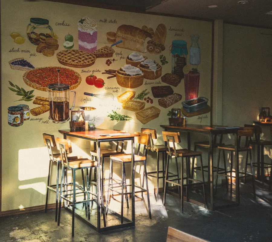 Tall café tables in front of a painted food mural, lit by low sun